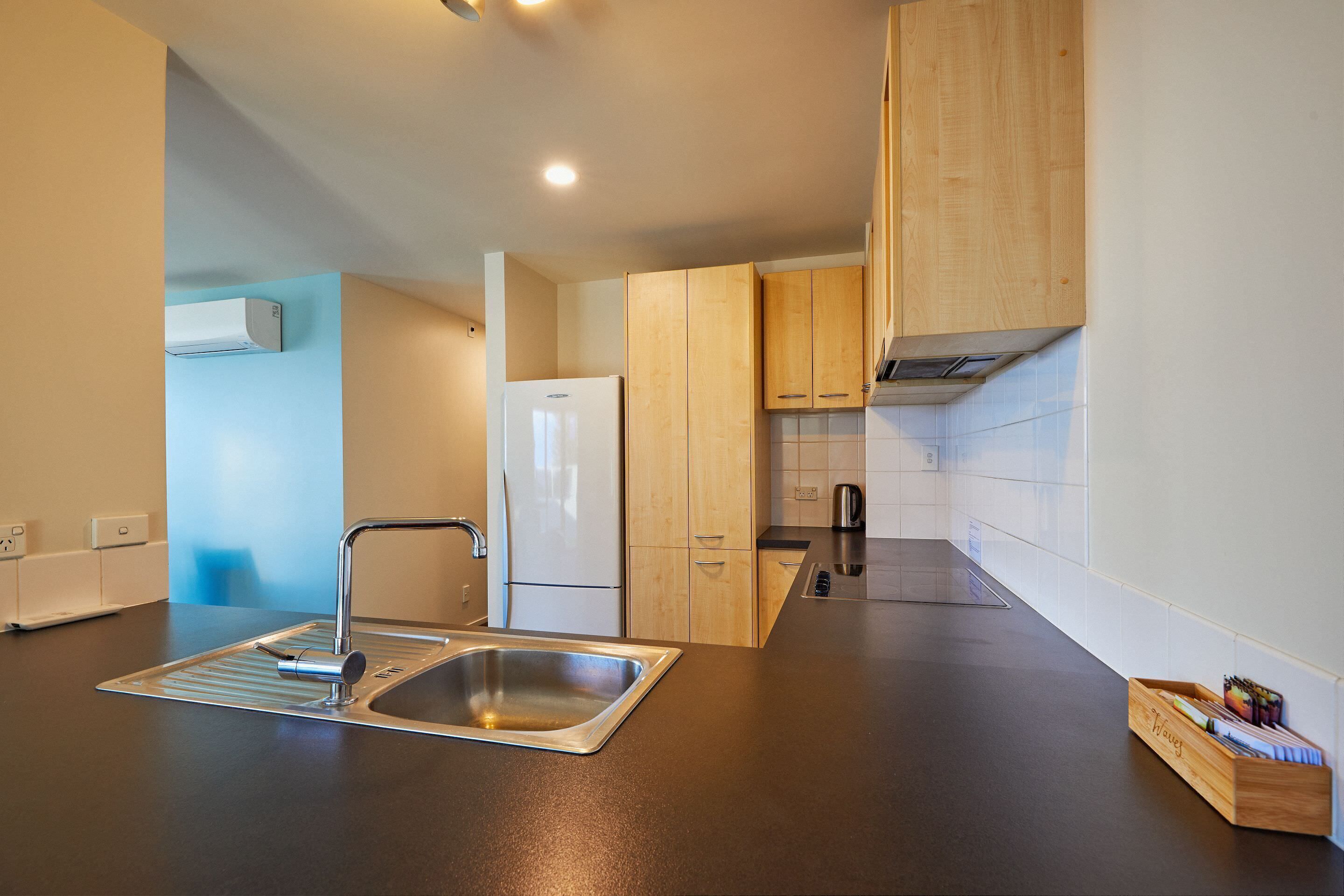 A modern kitchen with a stainless steel sink, wooden cabinets, a white refrigerator, and a tiled backsplash.