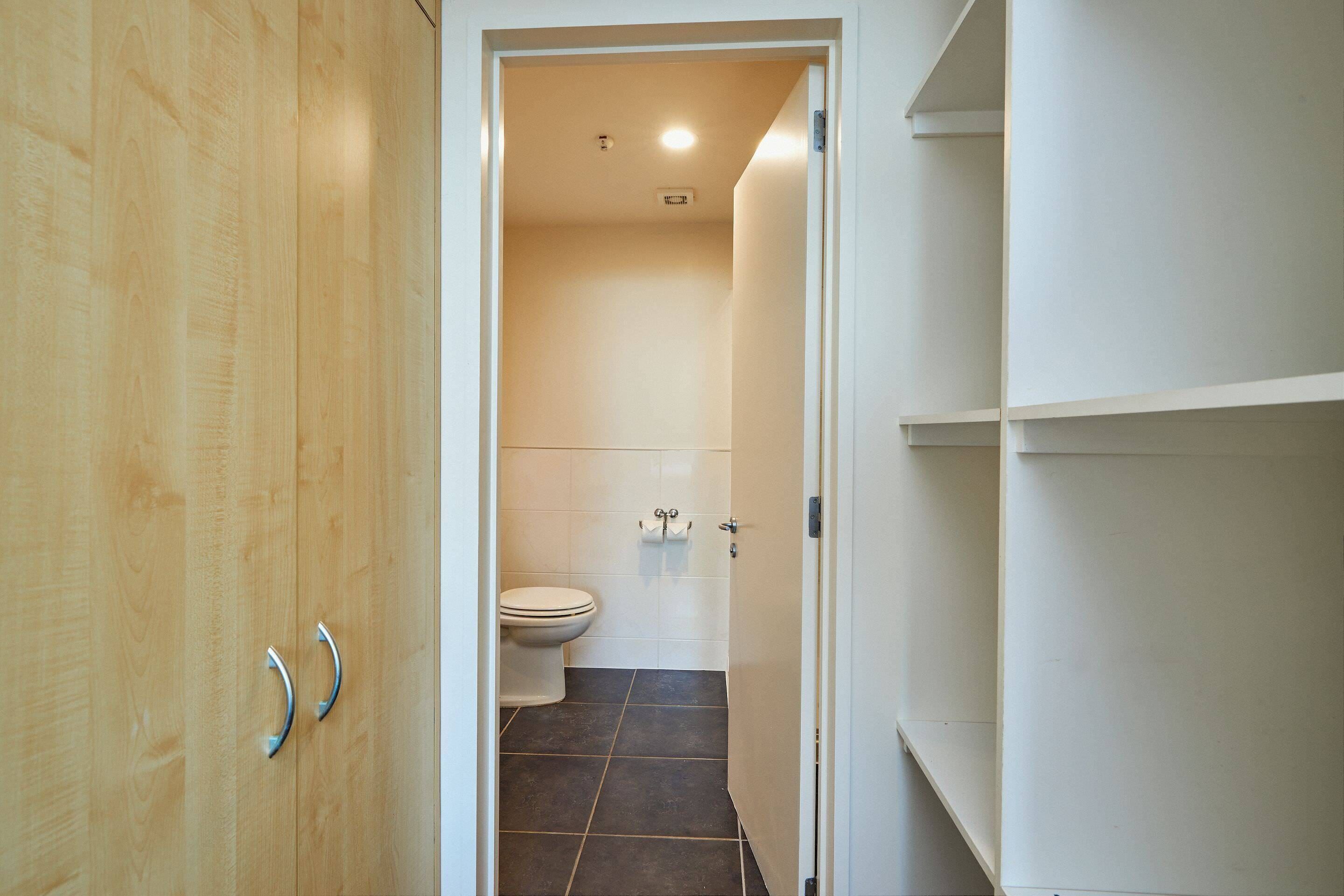 A bathroom with a toilet, dark tiled floor, and wooden cabinetry.