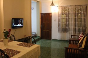 A living room with a television, a dining table with placemats, a sofa, and a door.