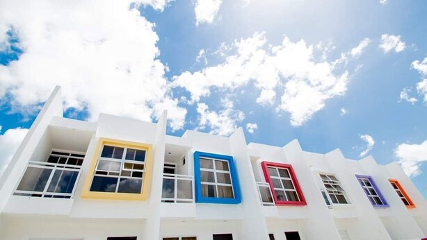 A row of white buildings with colorful window frames against a blue sky with clouds. - Townhome with 24Hr Security in Panglao Island (Dauis)
