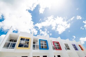 Una hilera de edificios blancos con marcos de ventanas coloridos contra un cielo azul con nubes.