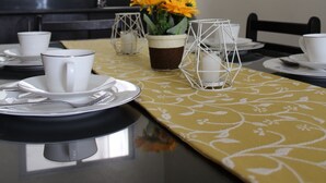 A modern kitchen with a dining area, featuring a kitchen island with a yellow patterned table runner, white cups, and a vase with yellow flowers. - Townhome with 24Hr Security in Panglao Island (Dauis)