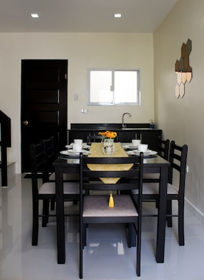 A dining area with a black table and chairs, a yellow tablecloth, and a vase with flowers.