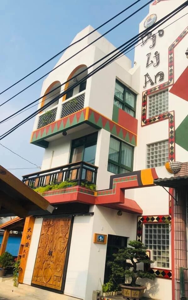 A multi-story building with a white facade, balconies, and a wooden door. - Dja Lji An Homestay (Sandimen)