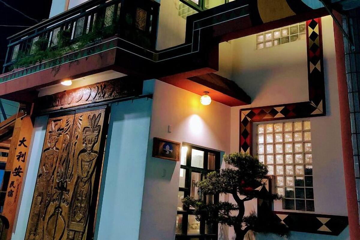 A multi-story building with a balcony, a large wooden door with carvings, and a small tree in front.