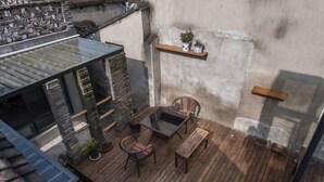 A wooden deck with a glass table and chairs, a stone wall, and a shelf with potted plants. - Zhenchuang Tingyu Pingjiang Inn No.2 (Suzhou)