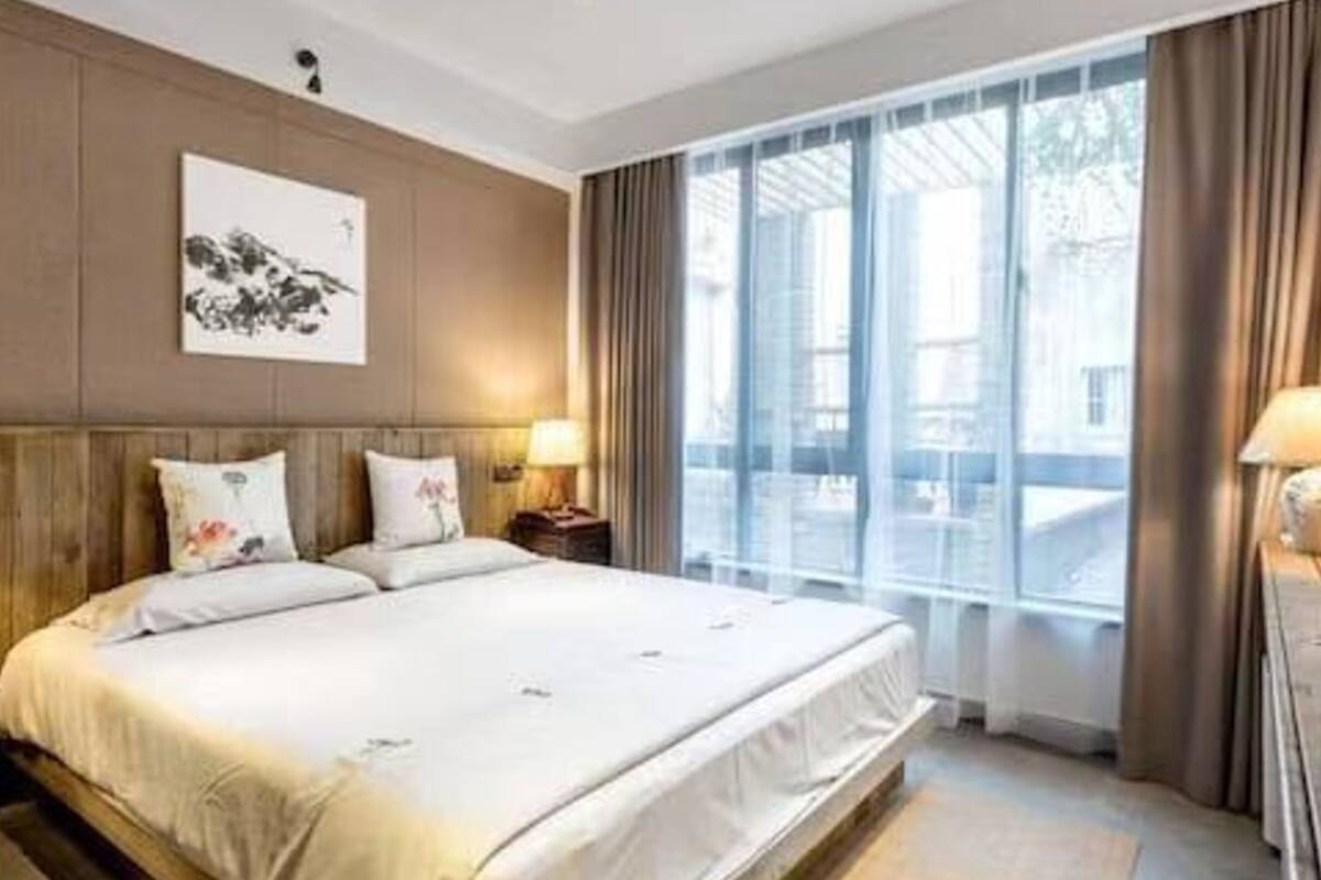 A modern hotel room with a large bed, a nightstand, a lamp, and a window with curtains.