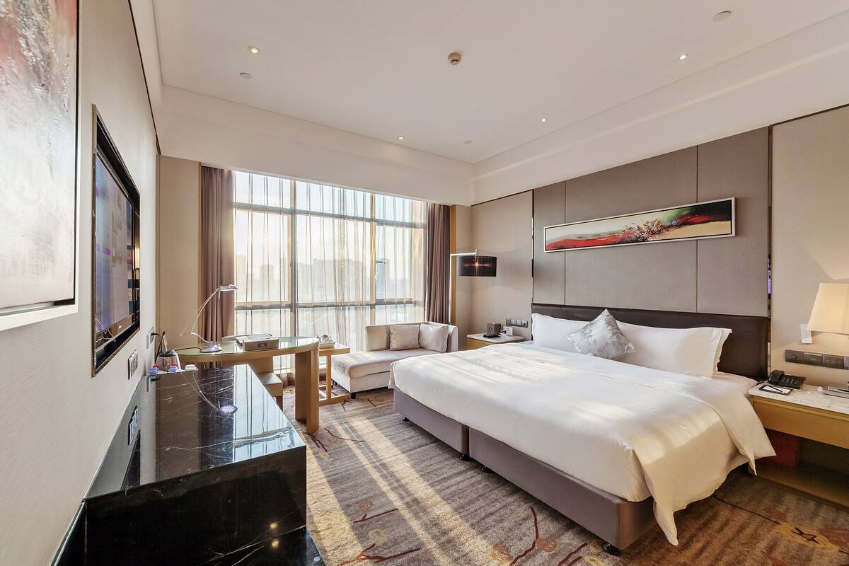 A modern hotel room with a large bed, a desk, a chair, and a TV.
