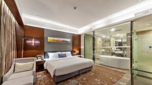 A modern hotel room with a large bed, a sitting area, a glass-enclosed shower, and a view of the bathroom. - Tianyuan Junlong Hotel (Xiamen)