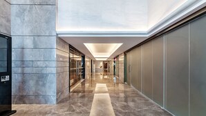 A modern hallway with marble floors and glass doors, leading to a central area with a ceiling light. - Tianyuan Junlong Hotel (Xiamen)
