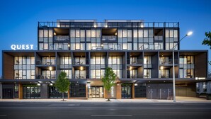 A modern multi-story building with the name "QUEST" prominently displayed. It features multiple balconies, large windows, and a clean, contemporary design.