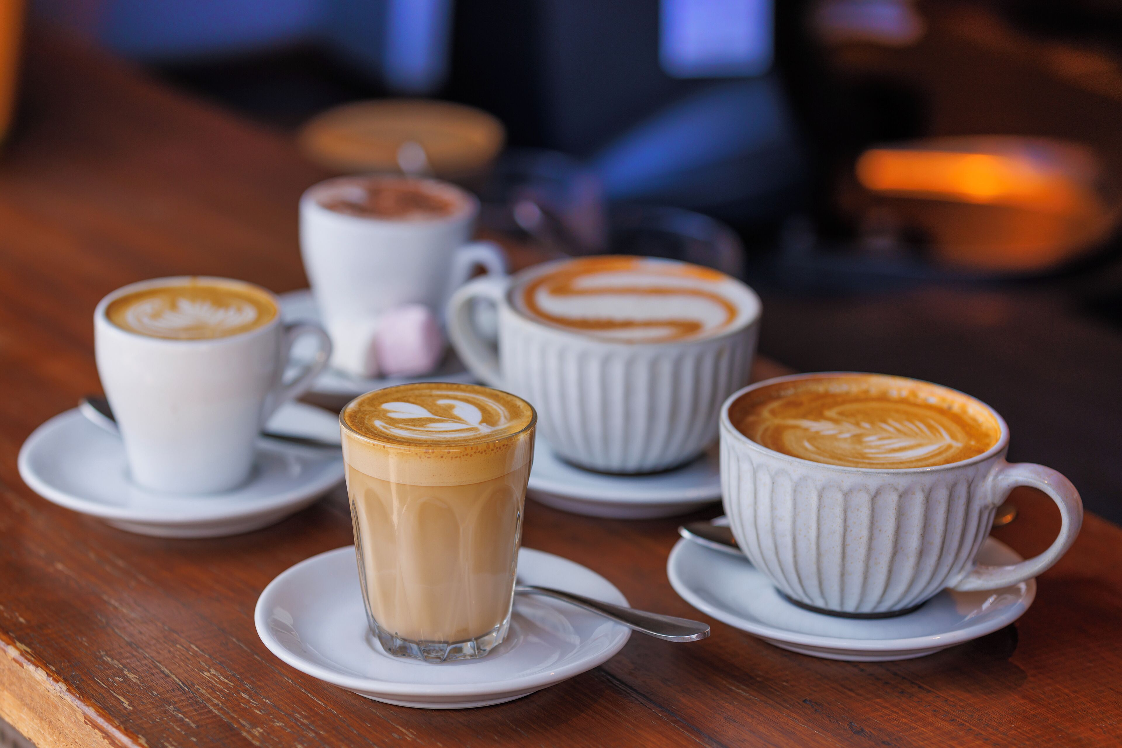 Una mesa con varias tazas de café, cada una con un diseño y decoración de arte latte diferentes.