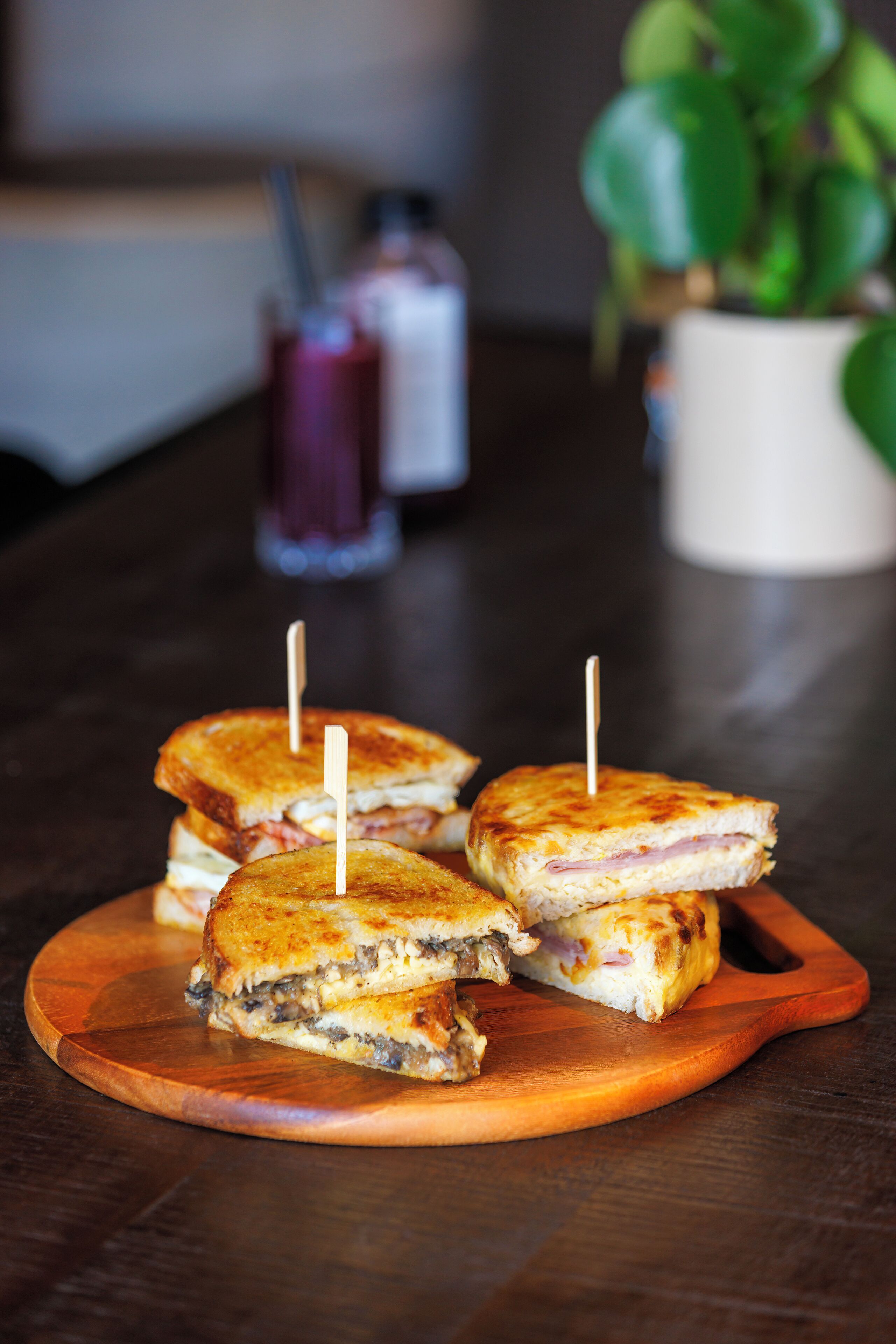 Una tabla de madera con sándwiches a la plancha, cada uno con un palillo.