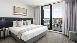 A hotel room with a large bed, a bedside table with a phone, and a view of the balcony.