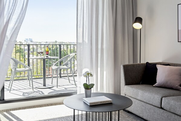 A modern living room with a sofa, a round table with a book, and a balcony with chairs and a table.