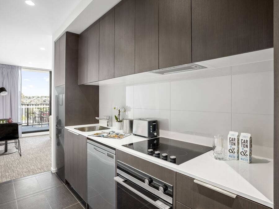 A modern kitchen with dark wood cabinets, a white countertop, a built-in oven, and a dishwasher.