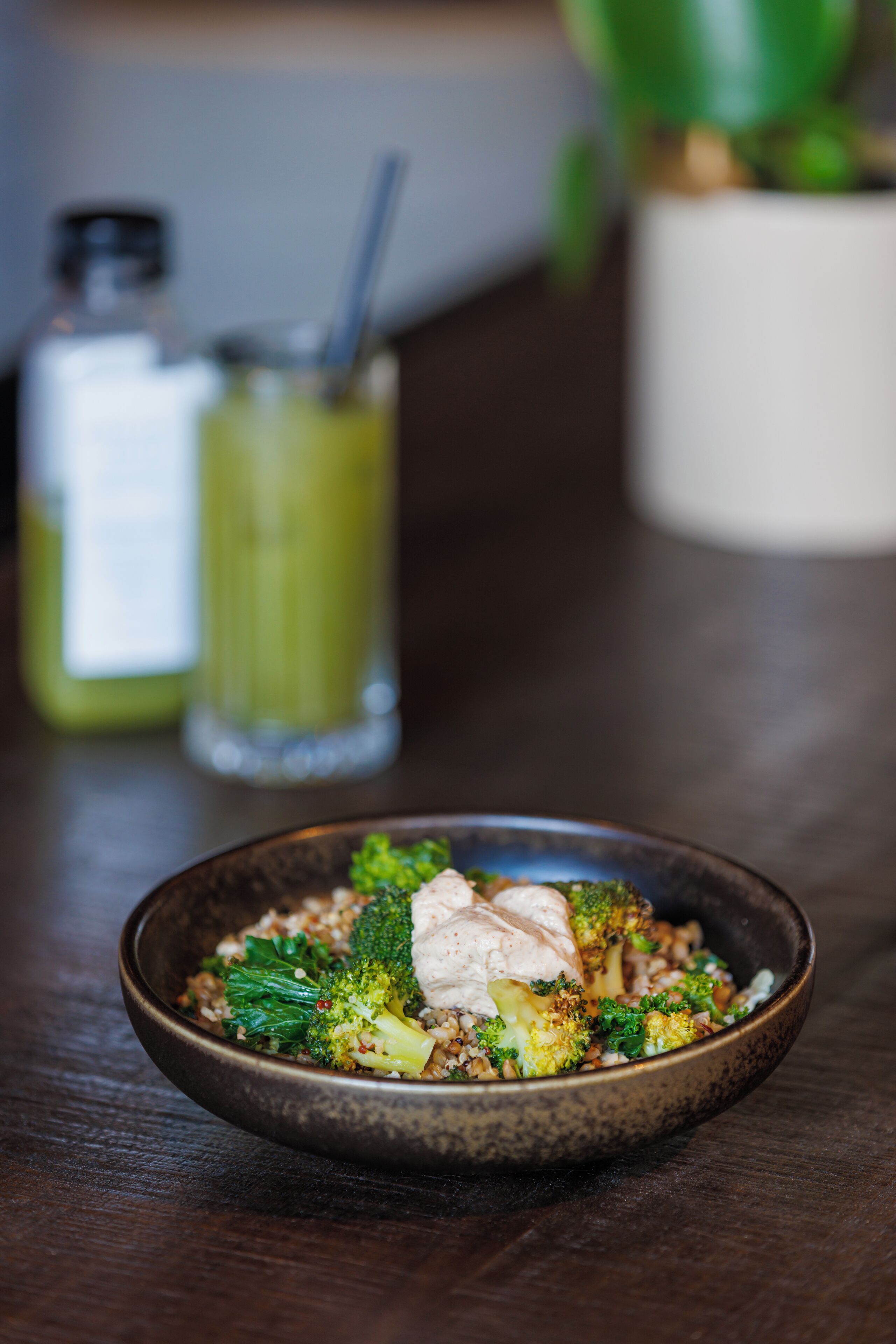 A bowl of food with broccoli and a white topping, placed on a wooden table.