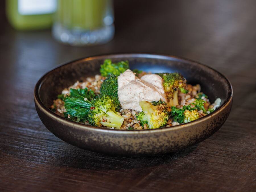 A bowl of food with broccoli and a white topping, placed on a wooden table.