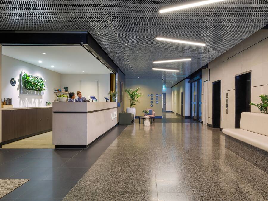 Un área de recepción moderna con mostrador, asientos y una pared verde.