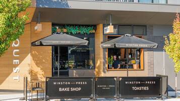 A modern building with a sign for 'Winston Press' cafe, featuring outdoor seating with umbrellas and a visible menu board.