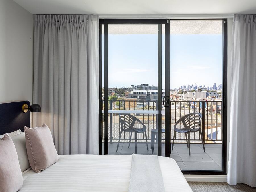 Une chambre d’hôtel avec un grand lit, une vue sur la ville depuis un balcon et un panorama urbain visible à l’extérieur.