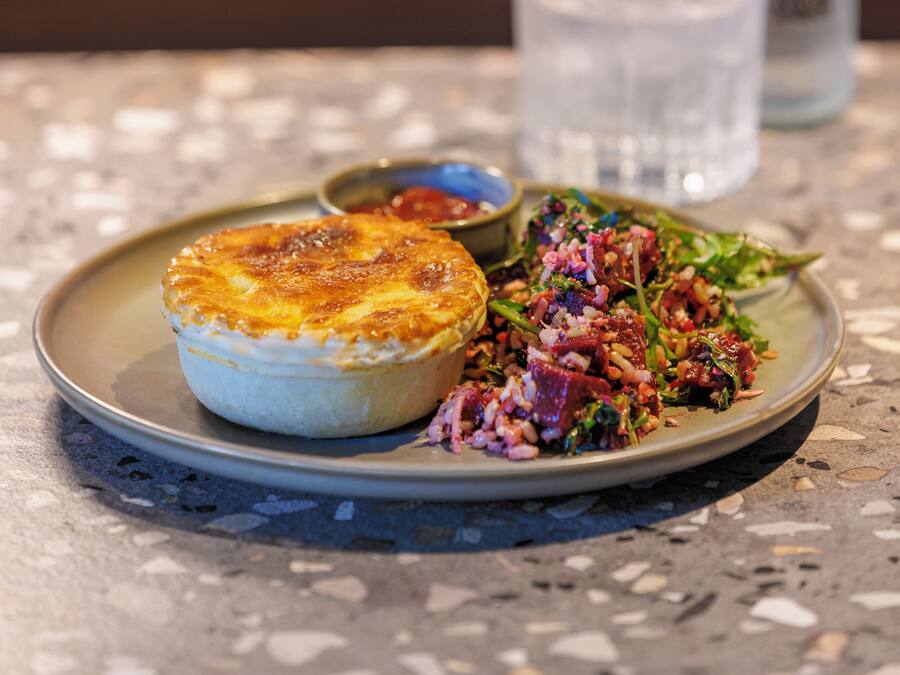 Um prato com um pastel e salada sobre uma mesa estampada.
