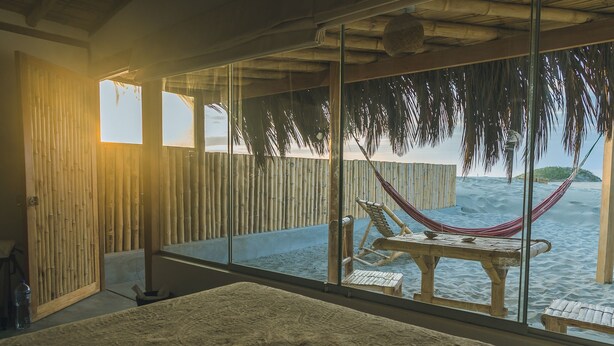 A room with a large bed, a wooden table with chairs, a hammock, and a view of the sea through large windows. - Vistazul (Los Organos)