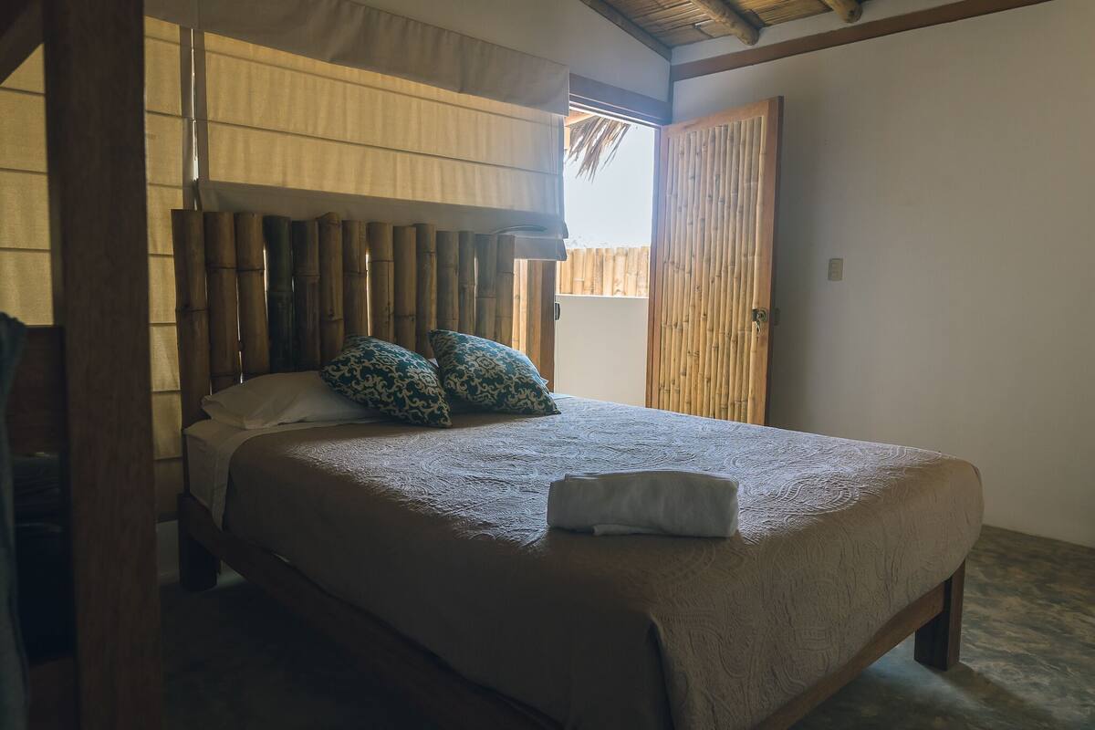 Un lit avec une tête de lit en bois, deux coussins à motifs et une serviette pliée.