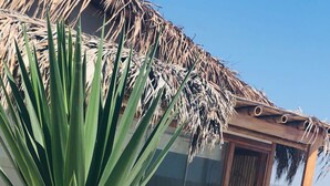 A beach scene with a palm tree in the foreground and a wooden structure with a thatched roof in the background. - Vistazul (Los Organos)