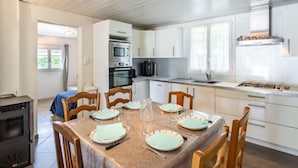 A modern kitchen with white cabinets, a dining table set for four, and a wood stove. - Pyrénées by Interhome (Capbreton)