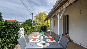An outdoor patio with a table set for four, surrounded by chairs, and a covered area with a roof. - Pyrénées by Interhome (Capbreton)