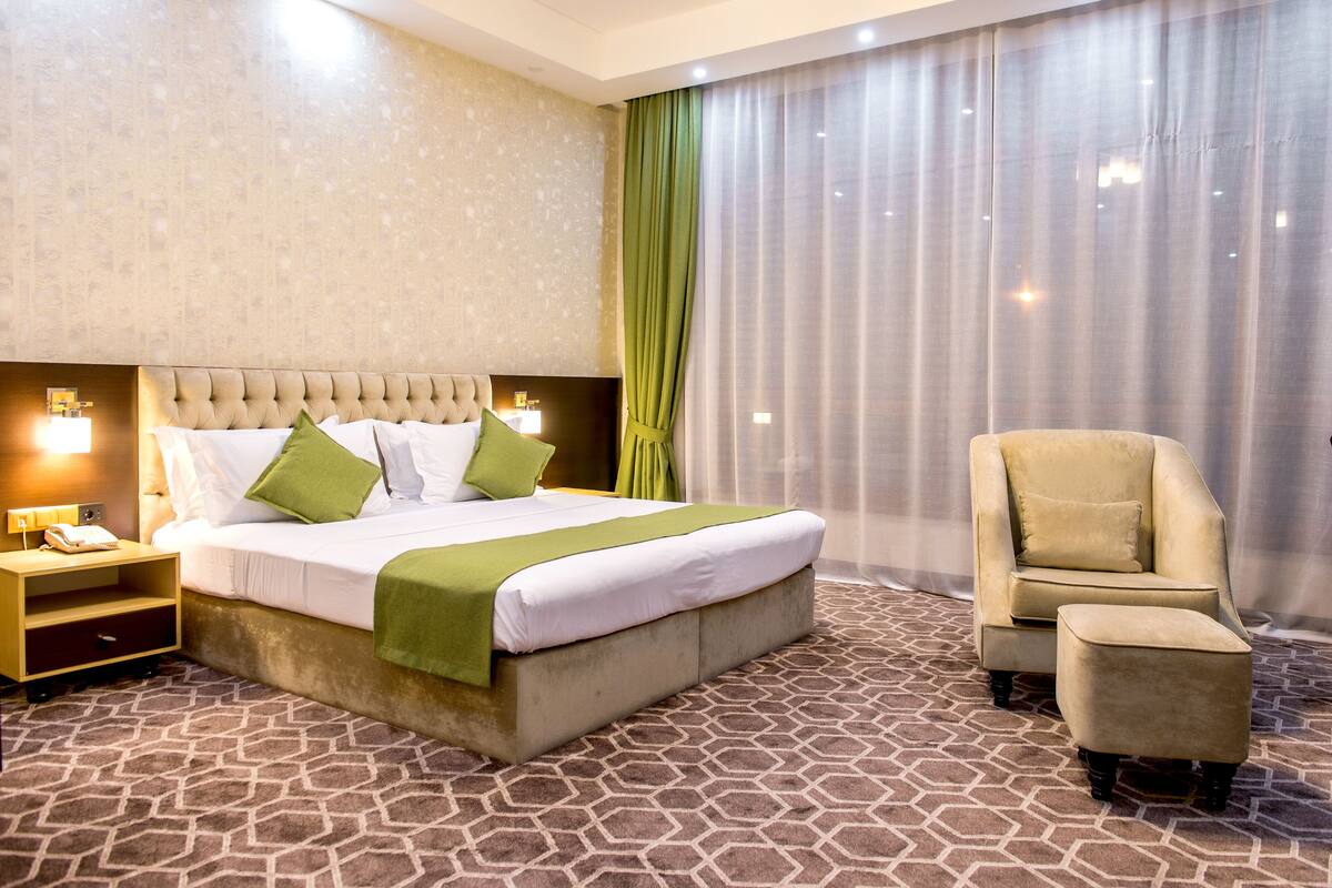 A hotel room with a large bed, a chair, a nightstand, and a patterned carpet.