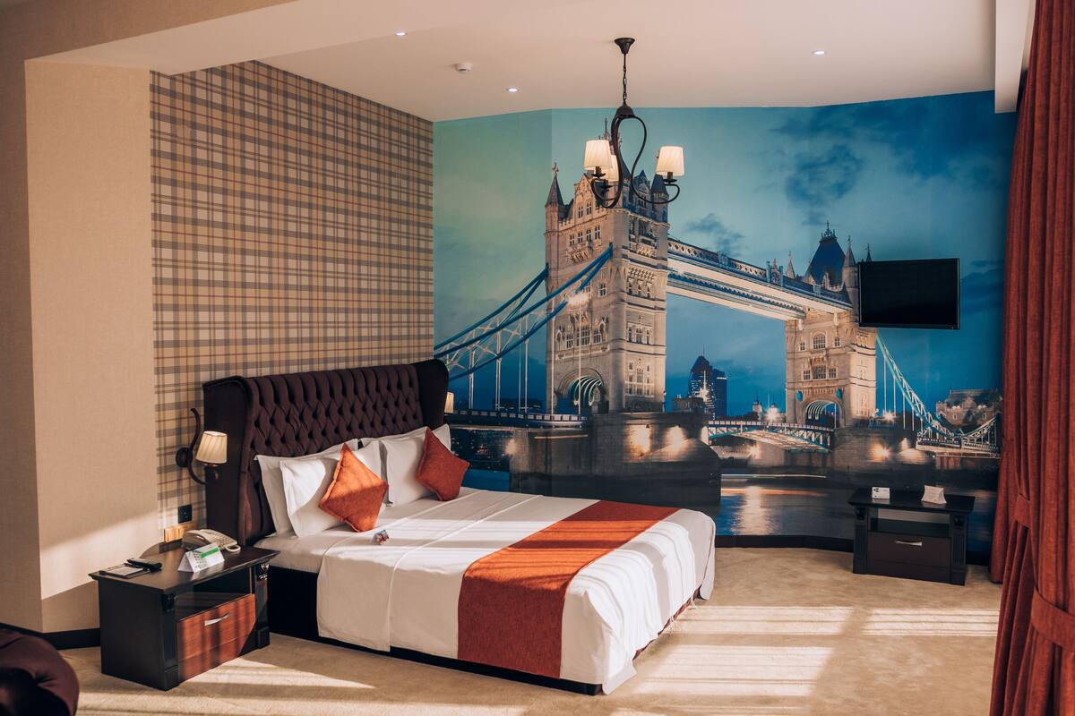 A hotel room with a large bed, a flat-screen TV mounted on the wall, a nightstand, and a desk with a lamp.
