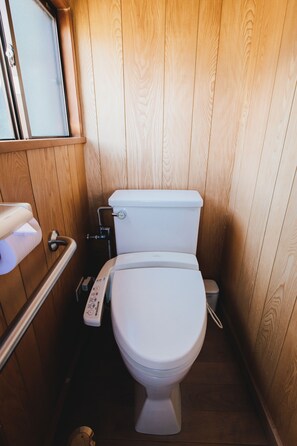 A compact wooden bathroom with a white toilet, a hand dryer, and a small trash bin. - Hostel Dockhouse (Nagasaki)