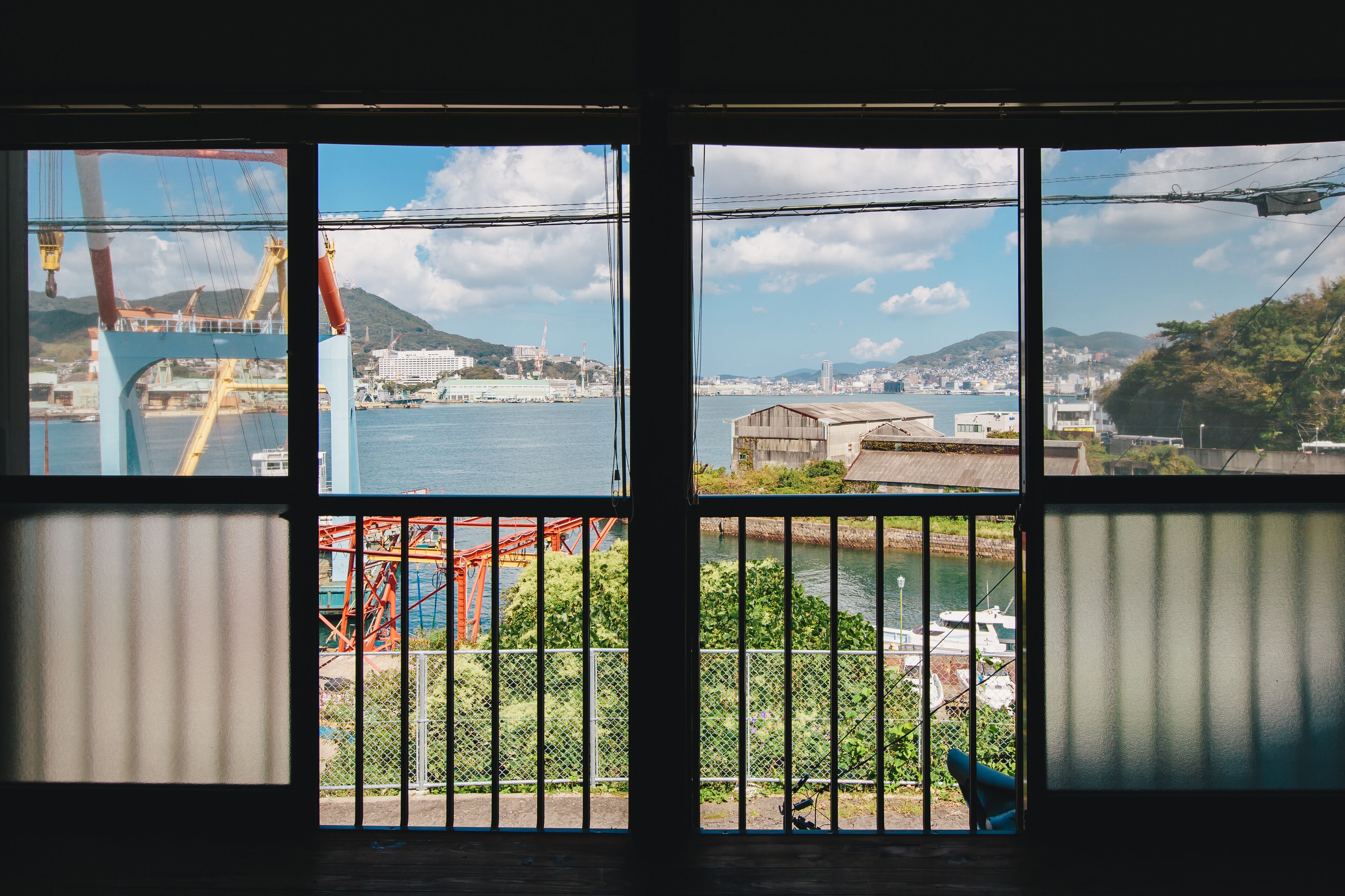 A view through a window with a metal railing, a body of water, and a distant cityscape.