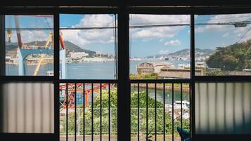 A view through a window with a metal railing, a body of water, and a distant cityscape.