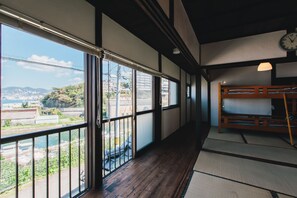 Ein Zimmer mit Holzboden, Tatami-Matten, einem Etagenbett und großen Fenstern mit Blick auf Stadt und Wasser.
