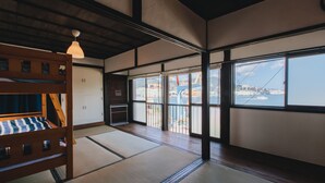 A traditional Japanese room with tatami flooring, a wooden bunk bed, and large windows offering a view of a coastal area. - Hostel Dockhouse (Nagasaki)