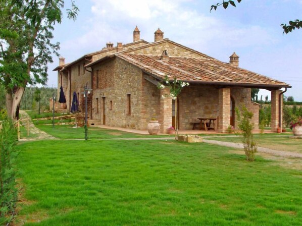 A stone building with a tiled roof, a covered patio, and a well-maintained lawn.