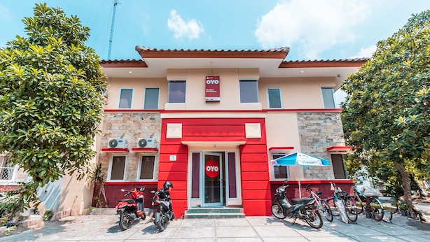 A building with a red and beige facade, a signboard, and several parked motorcycles. - OYO 1554 Pavilio  Residence (Cikarang)