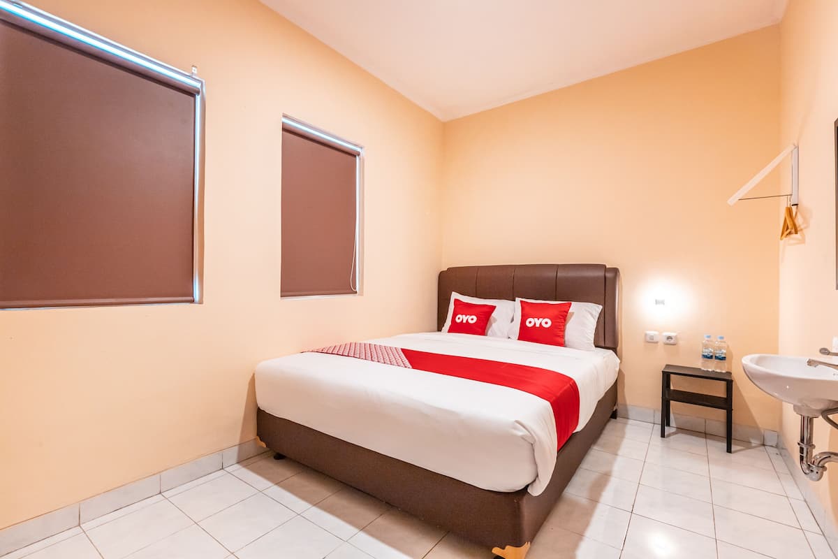 Habitación de hotel con cama, mesita de noche con botella de agua, lavamanos y ventana con persianas.