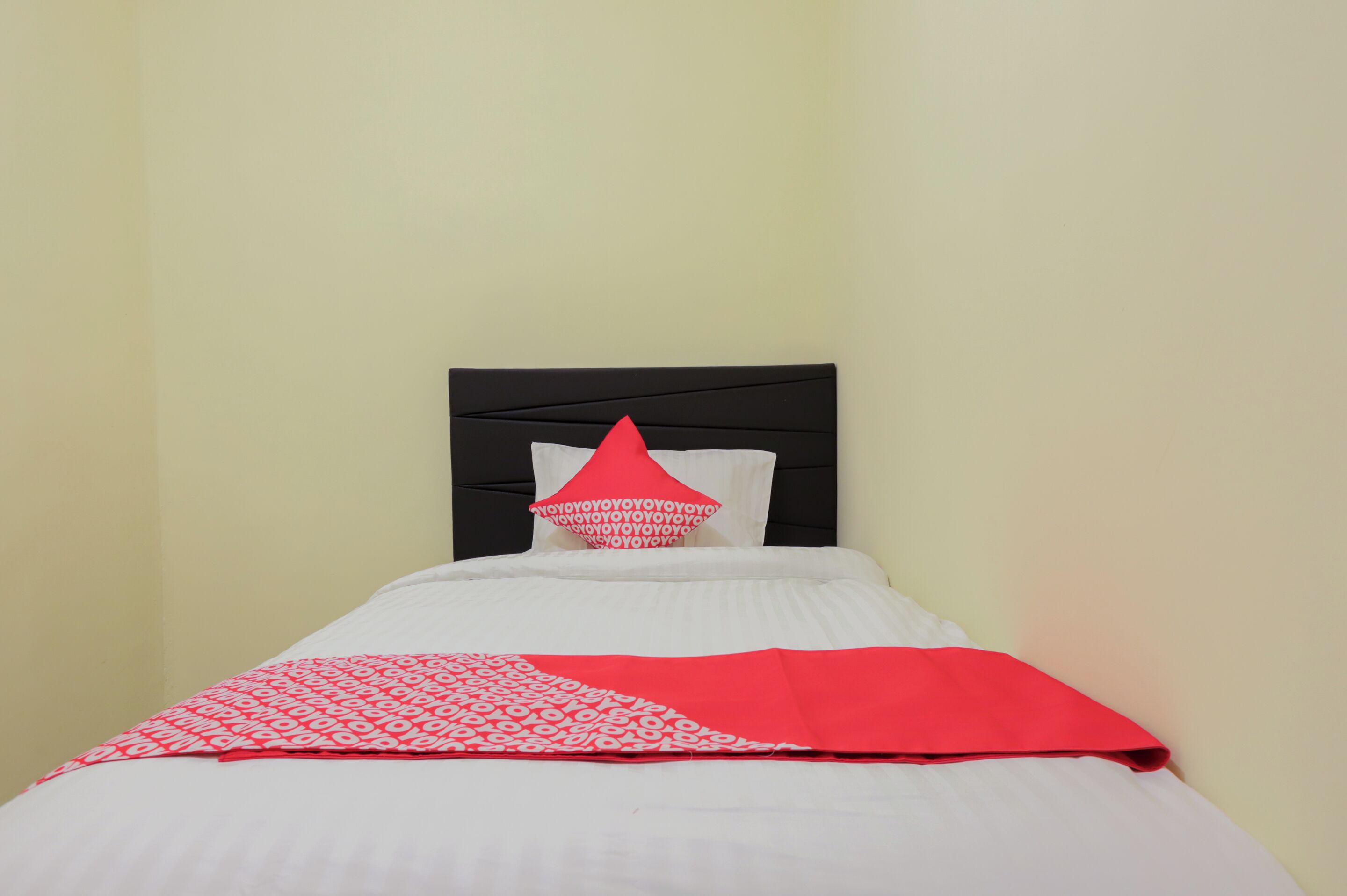 Una cama con cabecera negra, ropa de cama blanca y una colcha de diseño rojo y blanco.