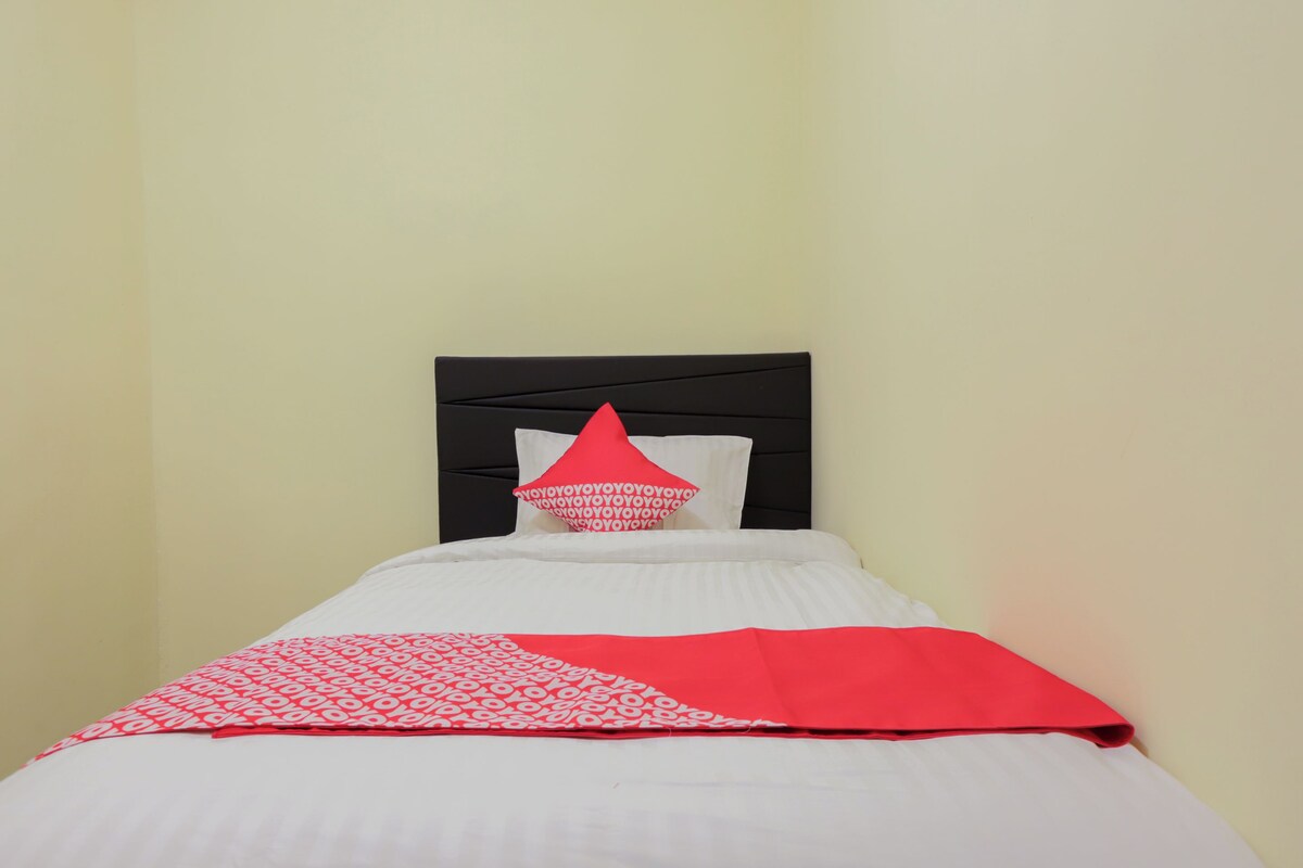 Una cama con cabecera negra, ropa de cama blanca y una manta con estampado rojo y blanco.