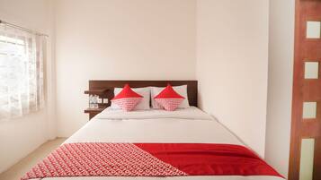 Una cama bien hecha con una colcha blanca y roja estampada, dos almohadas rojas y un cabecero de madera.