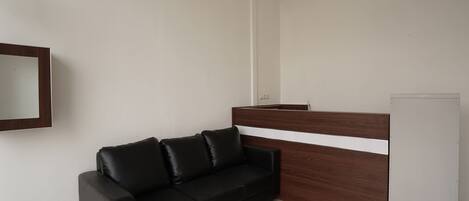 A modern room with a black leather sofa, a wooden reception desk, and a white refrigerator.