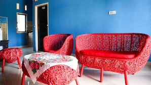 Una habitación con pared azul, una puerta con la etiqueta '108', y dos sillones de mimbre rojos con una mesa cubierta por un mantel floral.