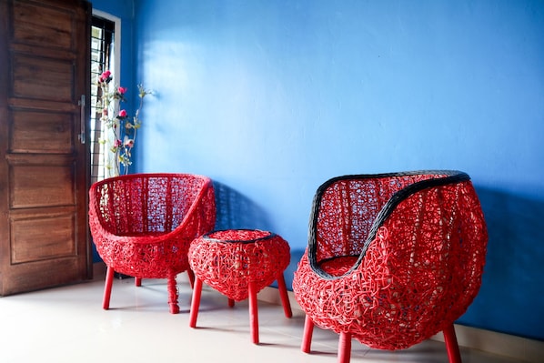 Two red wicker chairs with black accents and a small ottoman, positioned in front of a blue wall and a wooden door.