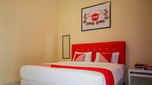Una cama bien hecha con cabecera roja y ropa de cama blanca, un cuadro en la pared y una mesita de noche.