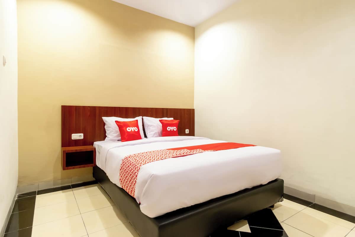 A hotel room with a bed, a wooden headboard, a bedside table, and a nightstand.
