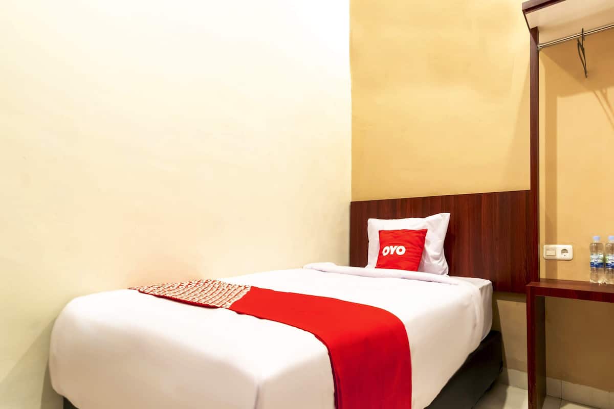 A hotel room with a bed, a wooden headboard, a nightstand with water bottles, and a red pillow with the logo "OYO".